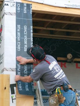 Apply side flashing from the top. First align the edge of the membrane with a pre-drawn pencil guideline on the housewrap measured to position the strip correctly, then peel away the backing and adhere the strip to the housewrap and sheathing.