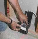 Here, a worker folds and tapes a precut piece of mass-loaded vinyl around a single-gang box. After the drywall is hung, each box should be sealed around the perimeter with acoustic sealant. When possible, outlets on opposite sides of a wall should be offset by at least three stud cavities.