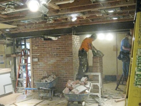 At this point, we were able to begin removing the bottom part of the chimney. The engineer had warned us to expect as much as 3/4 inch of deflection in the I-beams as they took the load. We gradually transferred the weight of the brick onto the steel by slowly lowering the 20-ton jacks we had used for temporary support. We worked our way around the chimney, first removing any loose shims, then removing loaded shims. When the final shims were removed, the beams had deflected about 3/8 inch, causing no damage to the tile and drywall finishes upstairs.