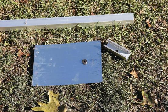 The rails are held off the roof at each connection by a short spacer or “mounting foot” cut from extra railing material. A manufactured aluminum flashing tab is slipped under the shingle above; its rubber grommet forms a weather­proof seal around the lag.