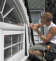 After fastening the lower trim layer in place with stainless-steel trim screws, a crew member scribes and fits additional PVC window trim and siding, and installs blocking to support the upper layer of trim.

