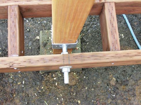 The bracket’s 3/4-inch-diameter saddle bolt must be securely fastened with a nut and washer on each side of the joist. Another post bracket (not visible in the photos) attached to a concrete pier keeps each post from contacting the ground. 