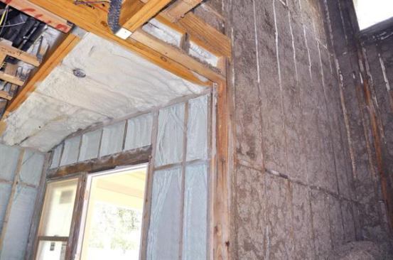 The 2x4 framing adjacent to the doorway has been sprayed with a thin layer of closed-cell foam, which will later be covered with a thicker layer of spray cellulose, already visible on the taller wall at right in the photo.