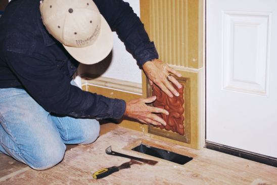 Composition ornament is a time-tested, fast, and inexpensive way to embellish interior finish details, such as this plinth block. It can be applied on site as seen here, or in the shop. Once installed, it finishes easily with minimal preparation.