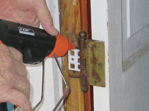 The kit has been helpful for tuning old windows and doors. Here, the author is gunning instant-tack adhesive to secure a hinge shim.