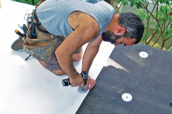 The upper edge of the first sheet of membrane is screwed to the deck at 12-inch intervals. A preprinted line 4 inches from the edge marks the correct overlap for the next sheet.