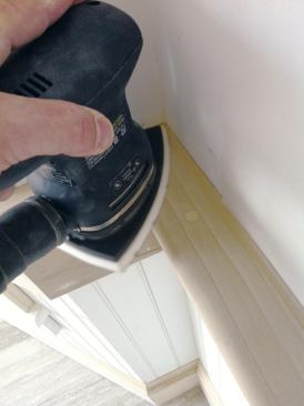 The author sands new trimwork with 120-grit paper before filling holes and priming. Good dust collection streamlines the process.