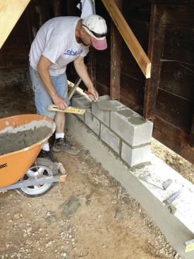 They retrimmed the existing studs to allow for two block courses and a 2-by PT mudsill, then installed the block, filling the cores.