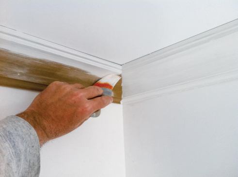 After patching nail holes and dings and sanding again, the author primes the trim.