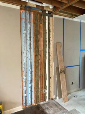 The steel angles are taped in place against the foam to protect the PEX lines, and the surrounding walls are insulated, ready for drywall.