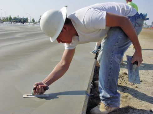 As the concrete becomes harder, switch to a smaller trowel (right hand) and continue increasing the blade angle to increase blade pressure to create a smooth and hard surface. In this image, you can see the larger trowel in the finisher’s left hand.