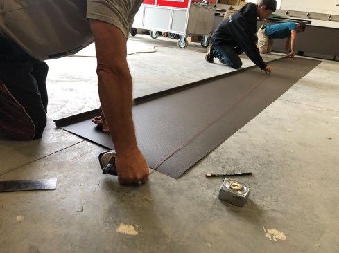 Workers ran a 228-inch-long section of coil stock through a standing-seam-roof-panel machine to form a female leg along one edge, then snapped a diagonal line on the pan following layout lines that they had already snapped on the floor