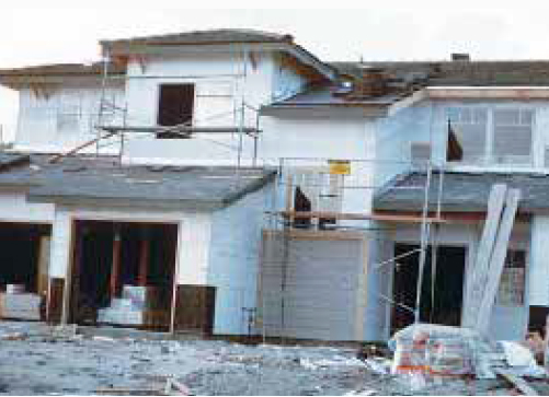 In House B, the builder chose to modify the small gable by making it a hip roof. That resulted in hip trusses running perpendicular to the shear wall. The carpenters made an effort to connect the strap to something solid by adding some blocking between the first two hip trusses.