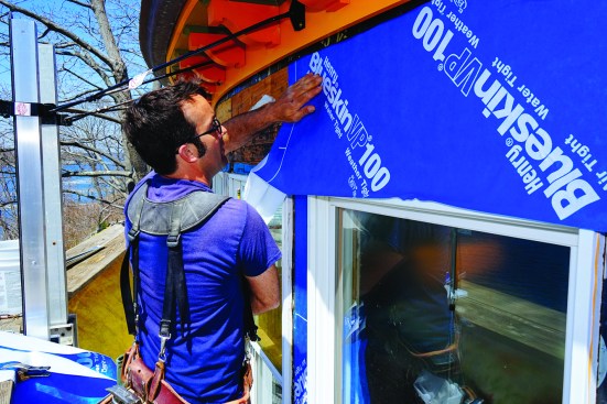 He peeled away the backing as he went and smoothing the pieces into position by hand. At the top of the wall, he left the existing curved soffit trim and bitumen–polyethylene membrane in place.