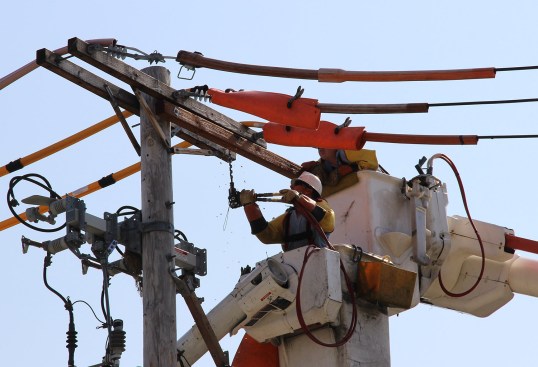 Utility workers maintain a power pole in Boston, Mass., in 2014. Power companies say homeowners with rooftop solar panels arenât paying their full share of the operating cost of the power transmission grid, even though they often draw power from the system.