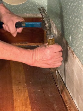 There wasn't enough space along the whole length of the wall between the last board and the wall to clear the tongue, so the author had to split off the tongue with a chisel.